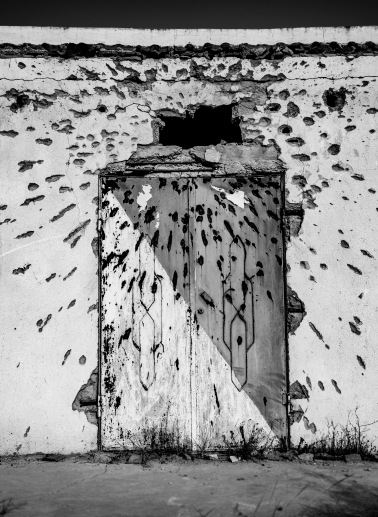A missile's impact on a wall and its shrapnel's around it has left the door without a lamp above it.